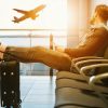 Calator relaxat in aeroport, cu bagajul langa el, privind un avion la decolare