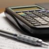 Calculator și pix așezate pe o foaie cu calcule