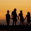 Siluetele unei familii care se ține de mână la apus